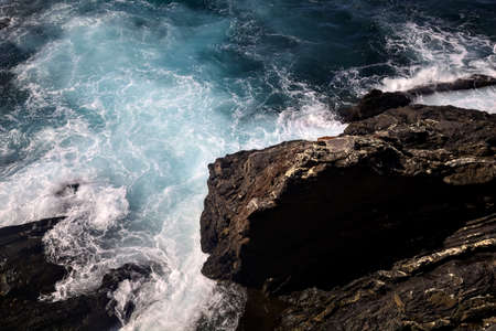 Waves crashing on the rocks of a cliff on a sunny day