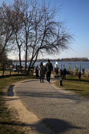 Path in a park by the shore of a lake with people strolling on a sunny dayの写真素材