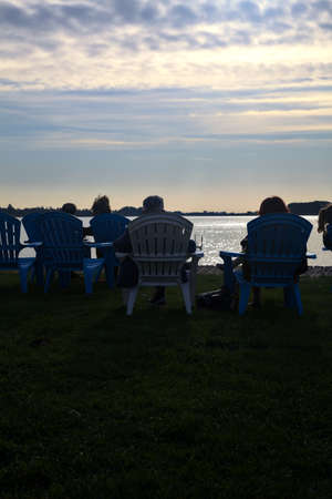 People laying on deck chairs by the lakeshore at sunset