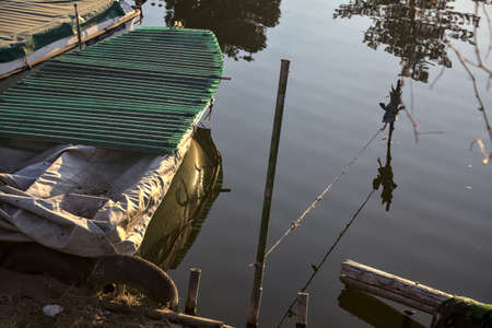 Moored boat and poles with their reflections casted in the water