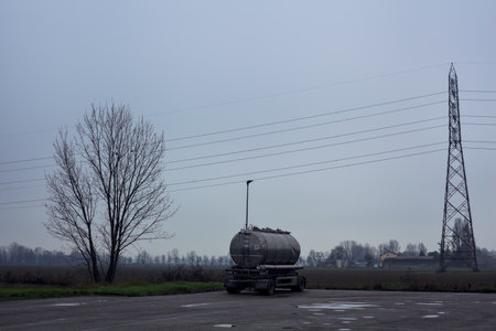 Tank in a parking lot by the edge of a fields with a pylon on a cloudy dayの写真素材