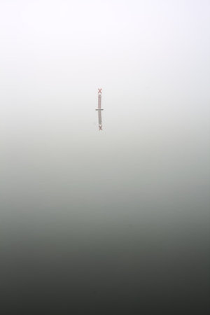 Pole on a lake on a foggy day in winterの写真素材