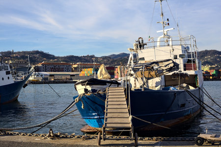 Docked fishing boats with flying bridges on the pier with a freight yard of an harbor in the distance at sunsetの写真素材