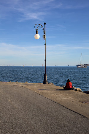 Pier with a girl sitting alone in the corner of a bend in it next to a street light at sunsetの写真素材