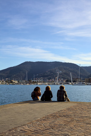 People sitting on the edge of a pier at sunset with mountain ridge in the backgroundの写真素材