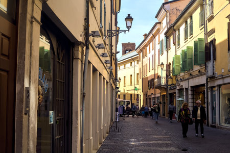 Narrow street in the shade with shops and people passing by on a sunny day in an italian town