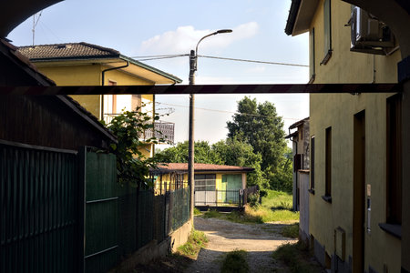 Covered alley between buildings that leads to a path next to a field on a sunny day in the Italian countrysideの写真素材