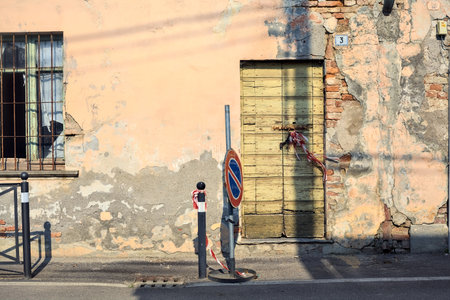 Pavement on a street bordered by a worn out facade with windows and wooden doors in a village in the Italian countrysideの写真素材