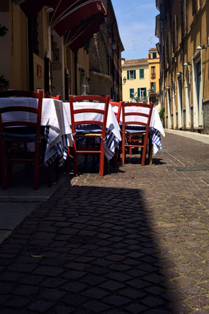 Alley partly in the shade with tables and chairs of a restaurant on a sunny day in an Italian townの写真素材