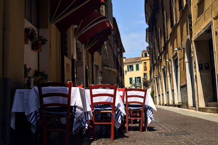 Alley partly in the shade with tables and chairs of a restaurant on a sunny day in an Italian townの写真素材