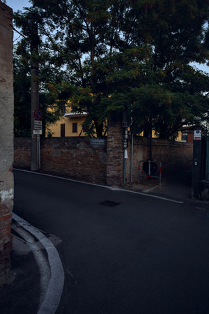 Entrance to a path by the edge of a road next to a brick wall with a tree arching on it at sunsetの写真素材