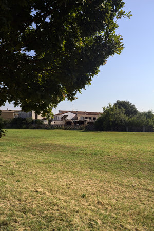 Country court and barn in a village seen from the opposite site of a field on a sunny day framed by a treeの写真素材