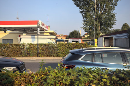 Msntova, Italy - October 2023 - Esso petrol station on a country road with a village and a chimney in the distance seen from behind a bush at sunsetのeditorial素材
