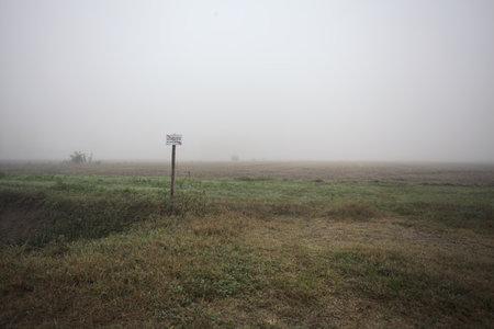 Entrance to a field with a sign over a trench coat on a foggy day in the Italian countrysideの写真素材