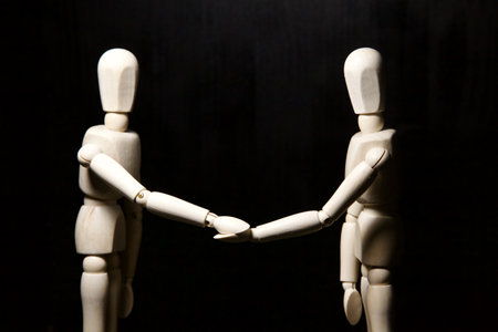 Two wooden figurines shaking hands on a black backgroundの写真素材