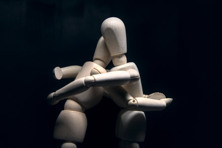 Two wooden figurines hugging each other on a black background