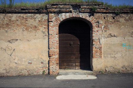 Boundary wall and wooden closed door of an abandoned building on a sunny day in an Italian townの写真素材