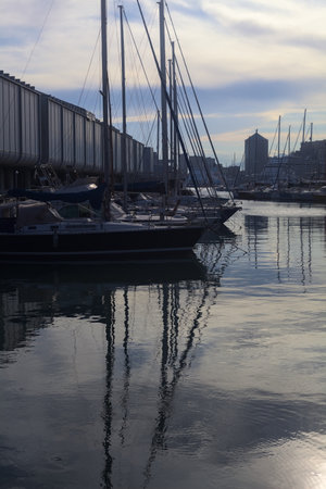Pier with buildings in a harbor with the sky and clouds cast in the waterの写真素材