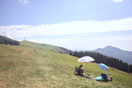 Grone, Italy -- August 2024 - People sunbathing and relaxing on a grassy plateau of a mountain