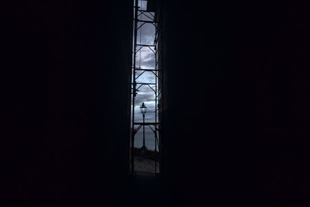 Narrow alley between tall buildings with a scaffolding hindering the sea at twilight in the distance