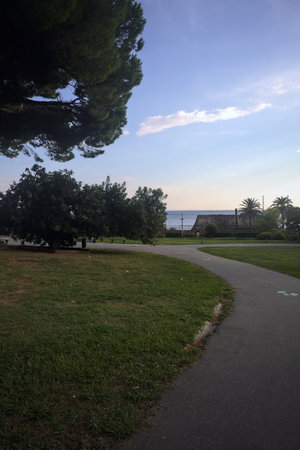 Path in a park next to a protective fence of a railroad by the sea at sunset
