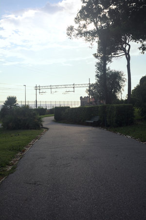 Path in a park next to a protective fence of a railroad by the sea at sunset