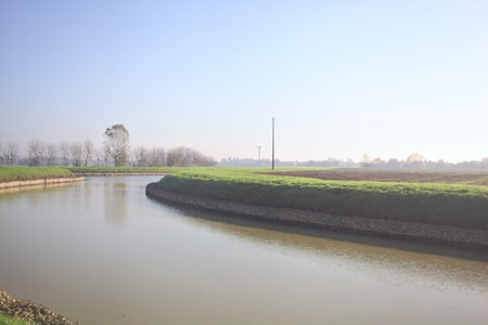 Diversionary channel bordered by trees and fields on a sunny day in the Italian countrysideの写真素材