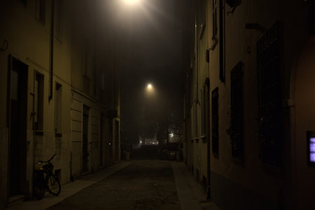 Narrow street on a misty night with hanging street lampsの写真素材