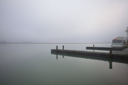 Pier casted on the water of a lake on a foggy day in the Italian countryside