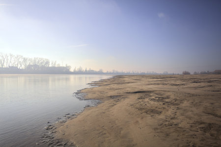 Embankment reflected in the water of a river seen from the opposite shore on a shoal