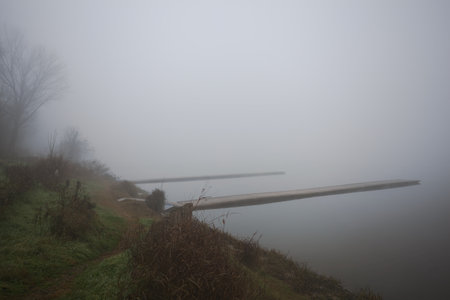 Piers next to a park by the lakeshore on a foggy morning in the Italian countrysideの写真素材