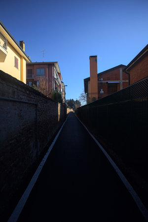 Path in the shade bordered by a fence and a brick wall in a residential area on a sunny morning