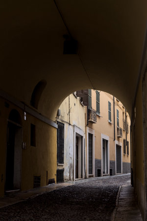 Narrow alley in the shade under an arch framed by a wall in an Italian townの写真素材