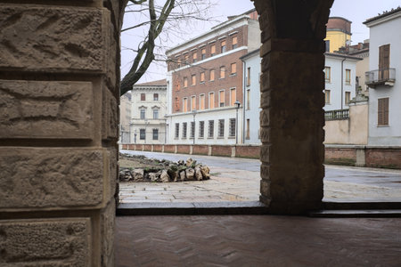 Promenade next to the edge of a garden with bare trees in an Italian town on a cloudy day seen from under a porchの写真素材
