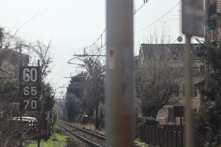 Railroad track with a sign by its edge and pillars with overhead powerline over it counterlit by the...