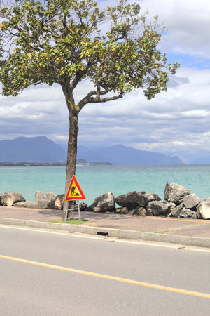 Road and promenade bordered by a breakwater and few trees by the lakeshore on a cloudy day
