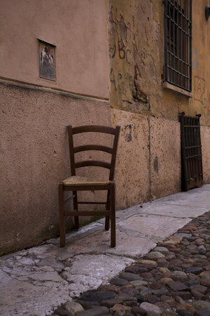 Wooden chair next to a wall on the pavement of a cobbled alley in an Italian townの写真素材