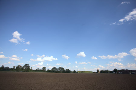 Plowed field with trees and buildings of a village in the background at sunset in the countrysideの写真素材