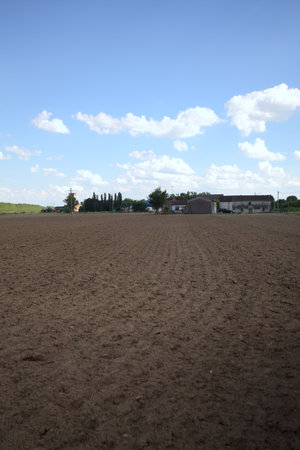 Plowed field with trees and buildings of a village in the background at sunsetの写真素材