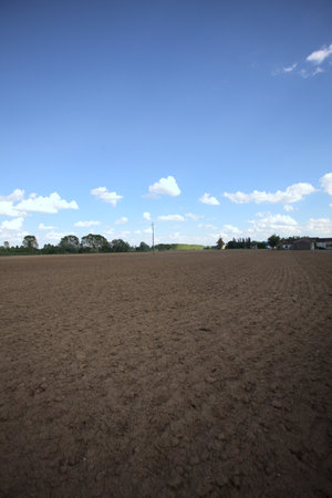 Plowed field with trees and buildings of a village in the background at sunset in the countrysideの写真素材