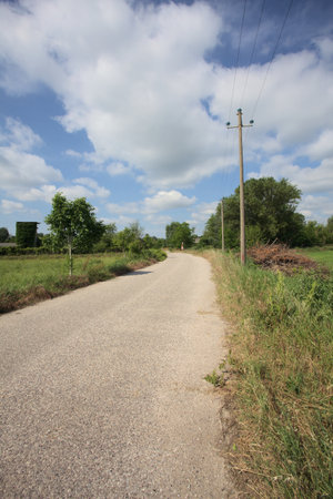 Dirt road between fields with an overhead power line by its edge blocked by a bar seen on a sunny day in the Italian countrysideの写真素材