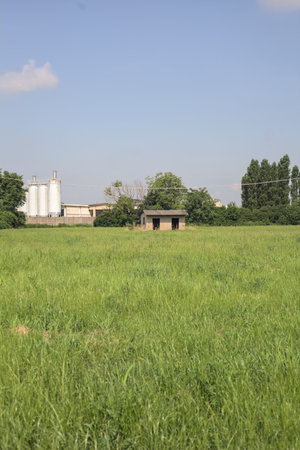 Abandoned concrete shack on a field with an industrial complex in the background on a sunny day in the Italian countrysideの写真素材