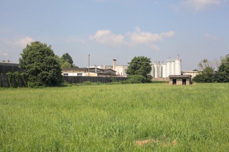 Abandoned concrete shack on a field with an industrial complex in the background on a sunny day in the Italian countrysideの写真素材