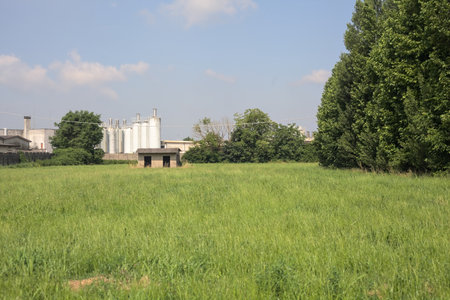 Abandoned concrete shack on a field with an industrial complex in the background on a sunny day in the Italian countrysideの写真素材
