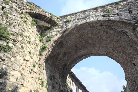 Stone arch of a bridge up above passing between walls with a partially cloudy sky as backgroundの写真素材