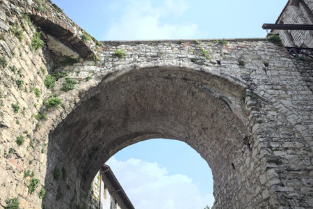 Stone arch of a bridge up above passing between walls with a partially cloudy sky as backgroundの写真素材