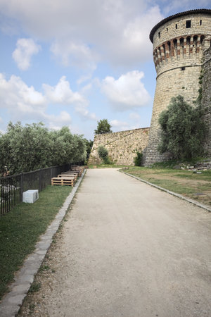 Path bordered by trees next to the wall of a castle inside its inner yard on a sunny dayの写真素材
