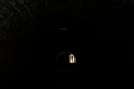 Arching passage in the dark with sunlight passing through holes and an opening in the distanceの写真素材