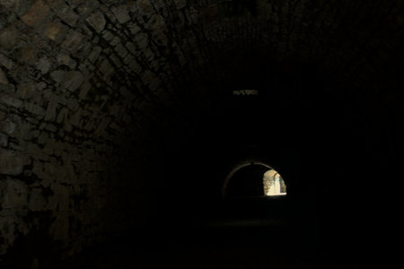 Arching passage in the dark with sunlight passing through holes and an opening in the distanceの写真素材