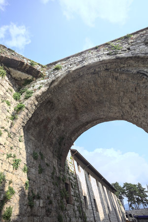 Stone arch of a bridge up above passing between walls with a partially cloudy sky as backgroundの写真素材
